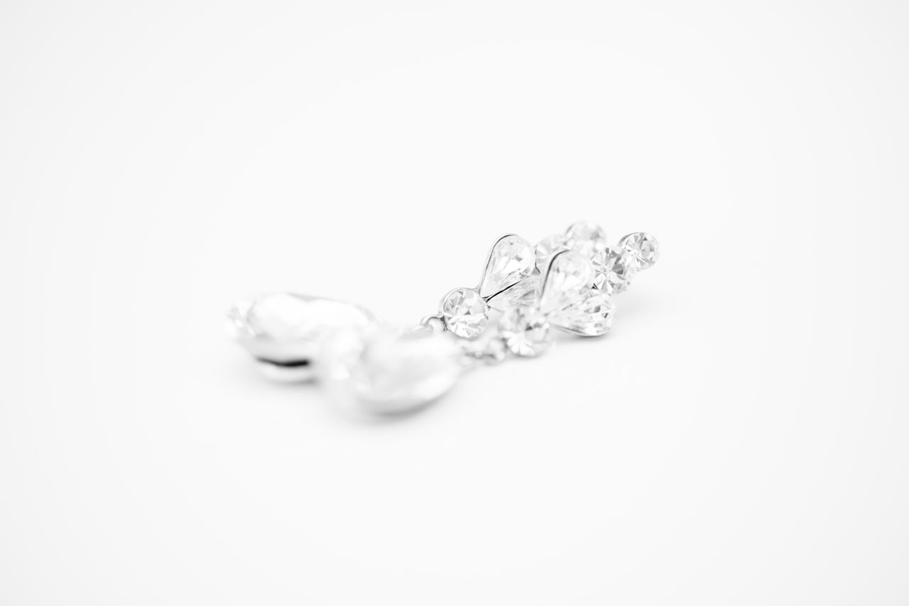 A black and white image of a pair of pearl and diamond drop earrings laying on a white surface.