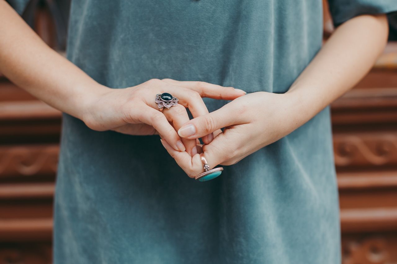 A woman standing with her hands together, showcasing her colorful rings.