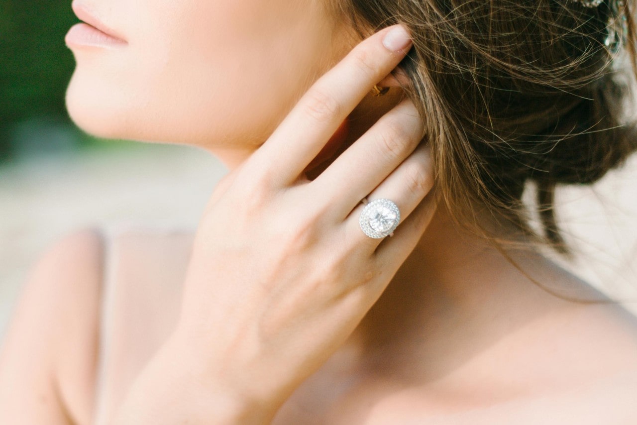 a woman with her hand in her hair, wearing a large halo engagement ring