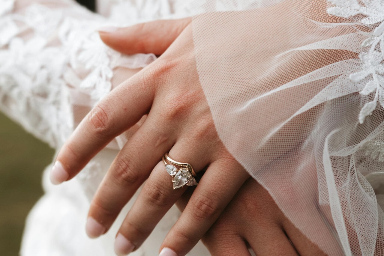 A close-up image of a bride’s hands wearing a three stone engagement ring and curved wedding band