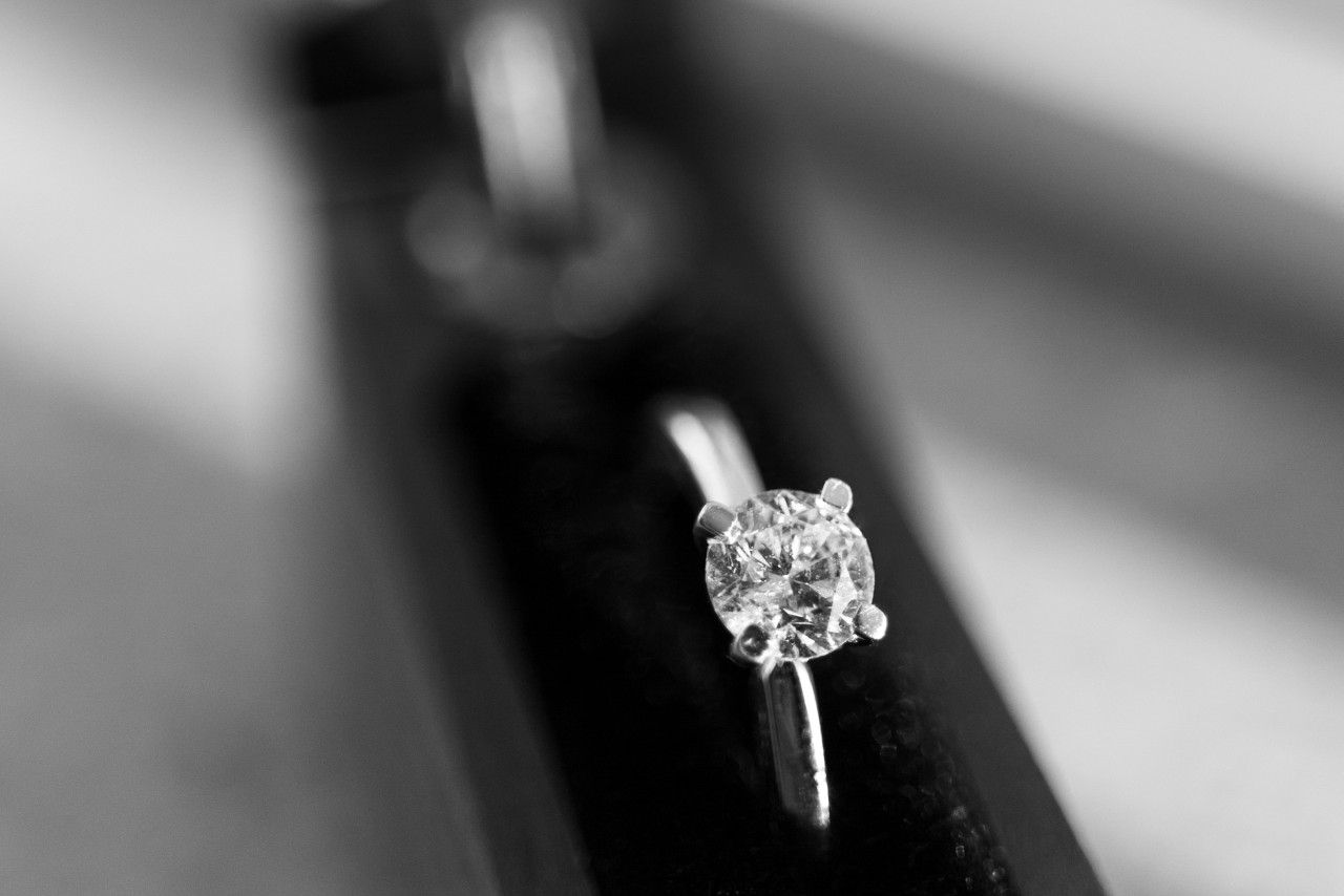 A close up of a black and white image of a solitaire engagement ring.