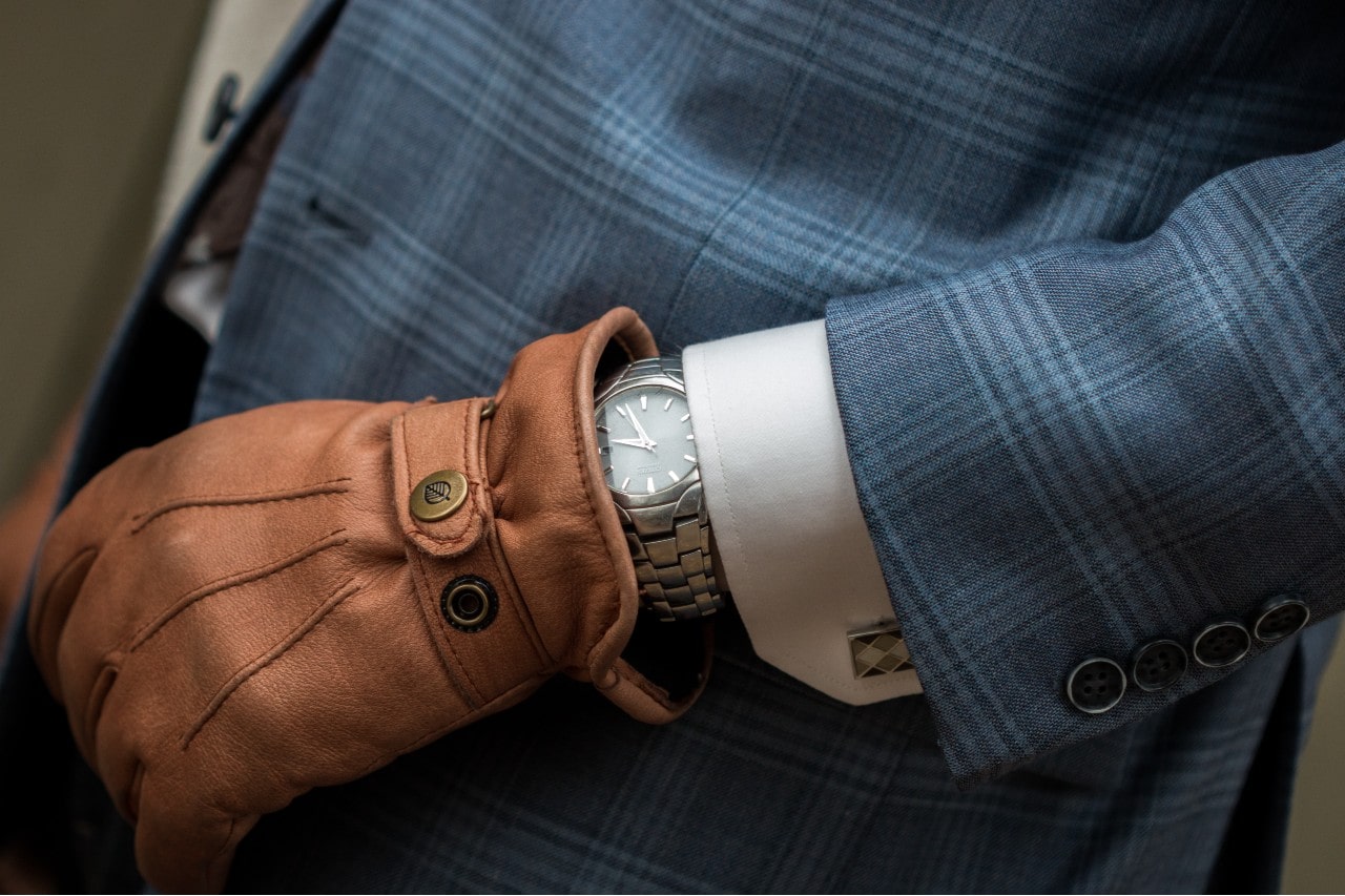 A man wearing a stainless steel watch with a blue checkered suit and leather glove.