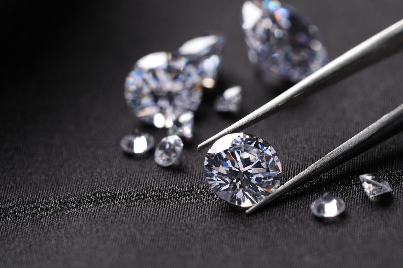 Several loose diamonds on a dark surface, one being picked by tweezers