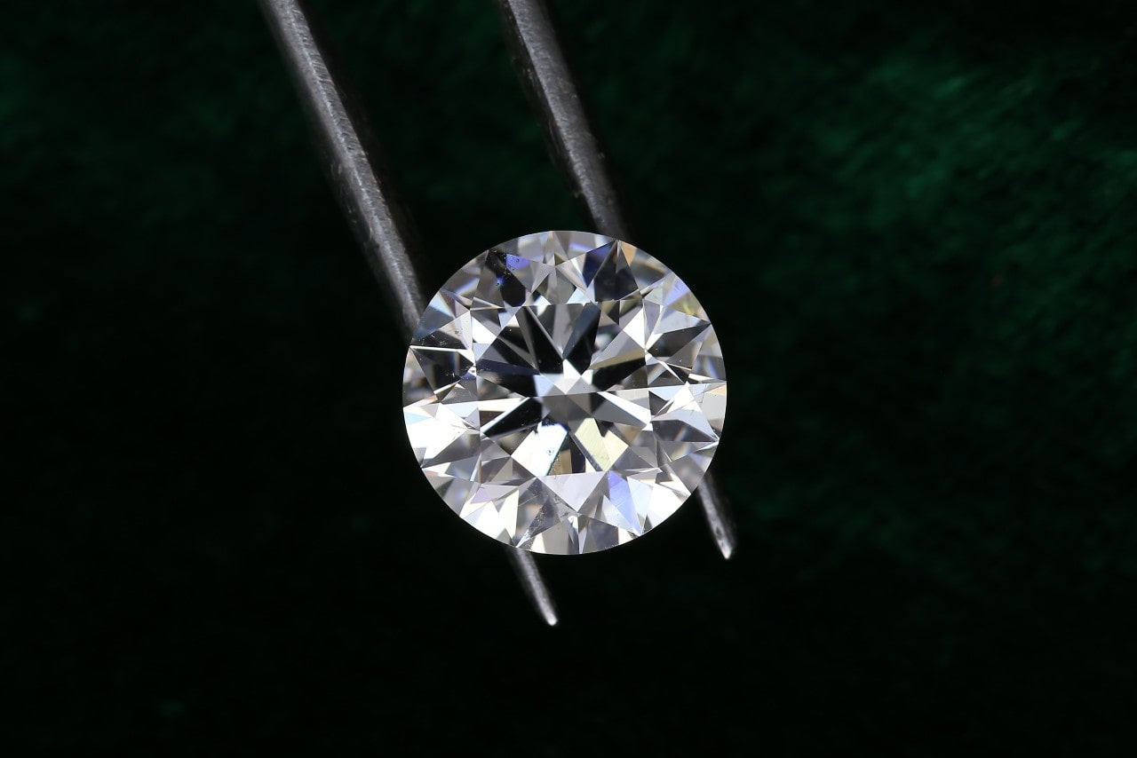 A close up of a round cut diamond being held by tweezers