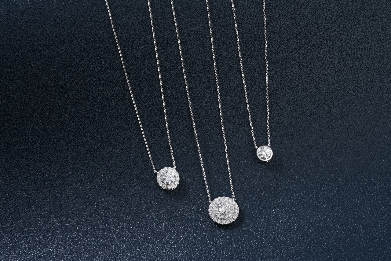 A close-up of three silver diamond pendant necklaces on a black surface.