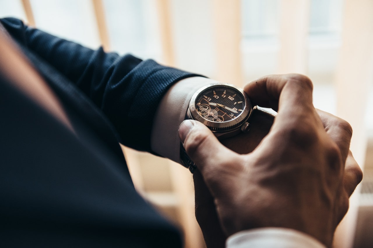 A close-up of a man in a suit looking down at his mixed metal watch.