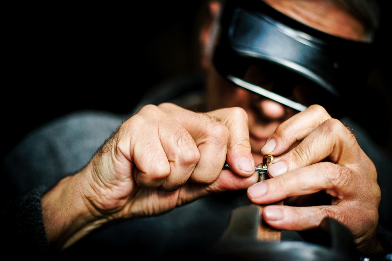 A close-up of a jeweler wearing protective eyewear repairing a gold band.