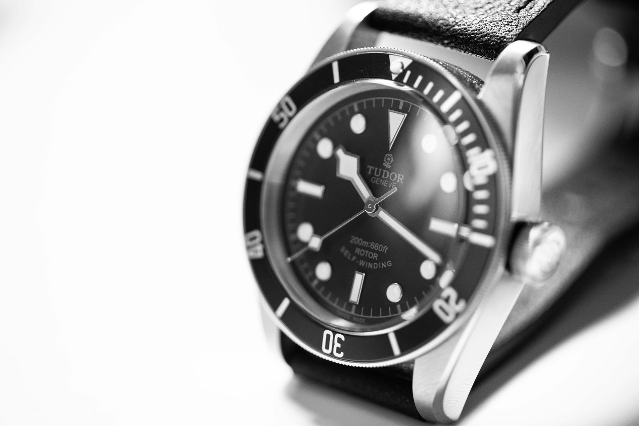 A black and white close up of a TUDOR watch with a white backdrop.