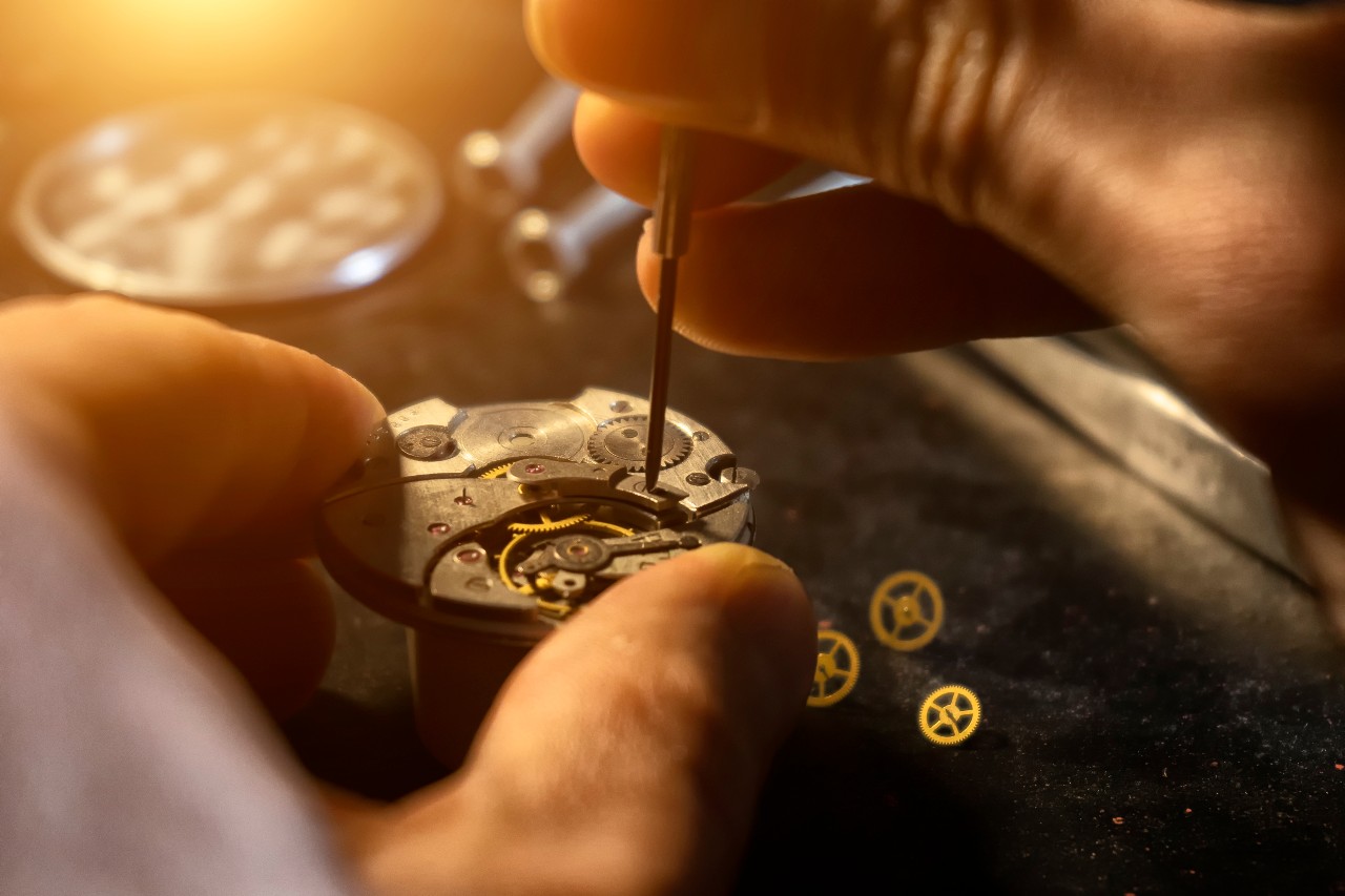 A close-up of a watchmaker’s hands adjusting the gears of a mechanical watch under warm lighting.