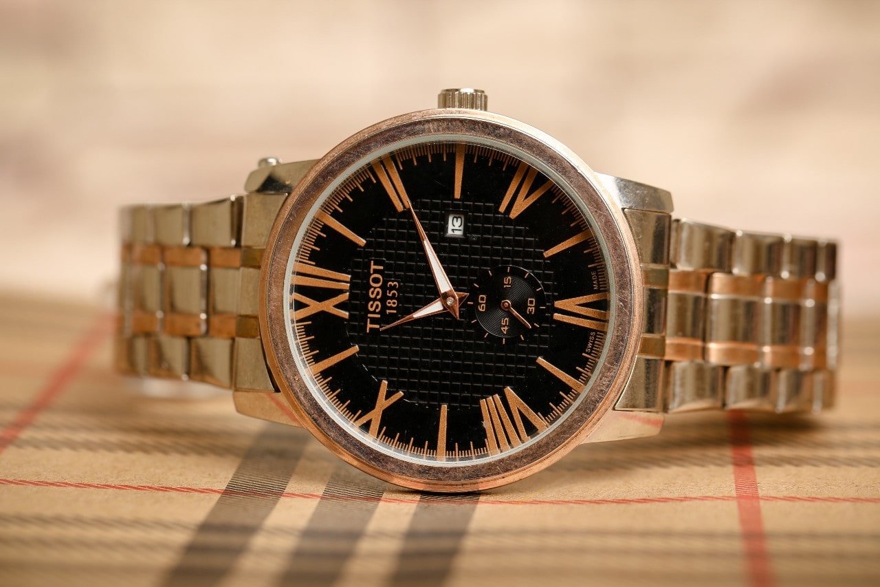 A close up of a gold plated Tissot watch with black dial and matching bracelet.