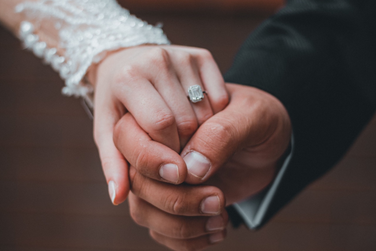 A couple in their wedding attire holding hands, showcasing the bride’s emerald cut engagement ring.