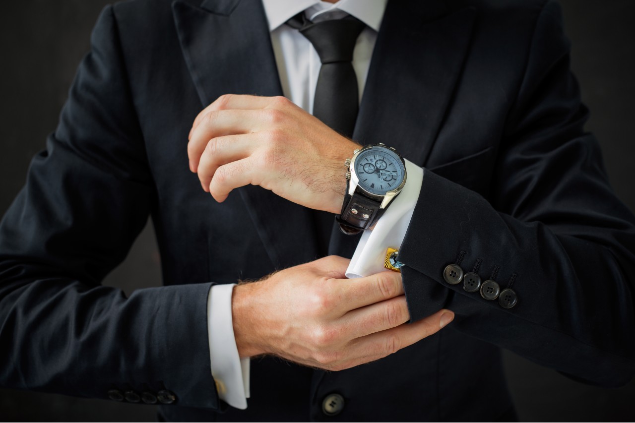 A close-up of a well-dressed man in a suit adjusting his cuff just below his luxury watch.