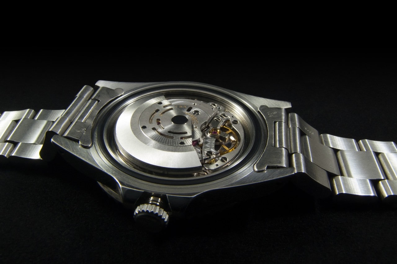 A close-up of a luxury watch on a black backdrop, its back open in preparation for maintenance.