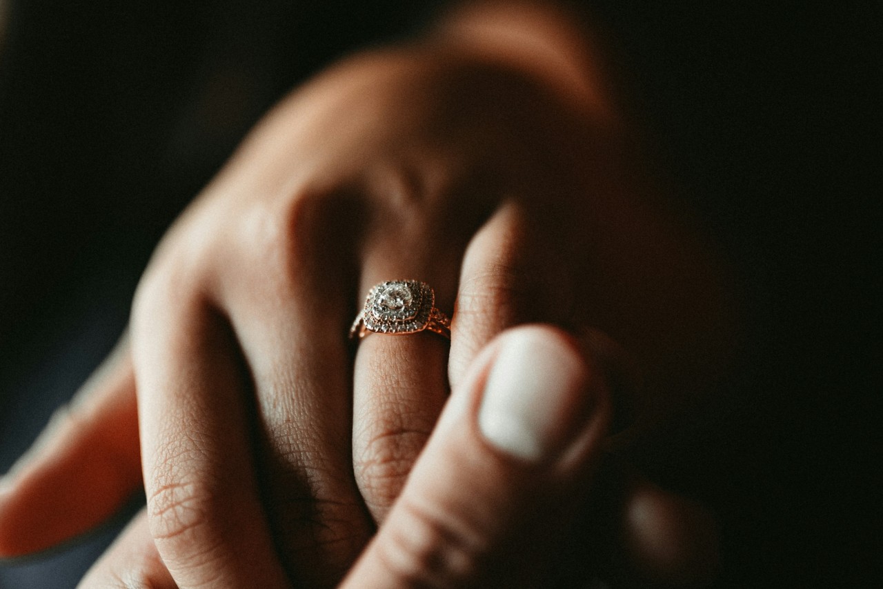 A close up of a woman’s hand with a rose gold double diamond halo engagement ring on her finger.