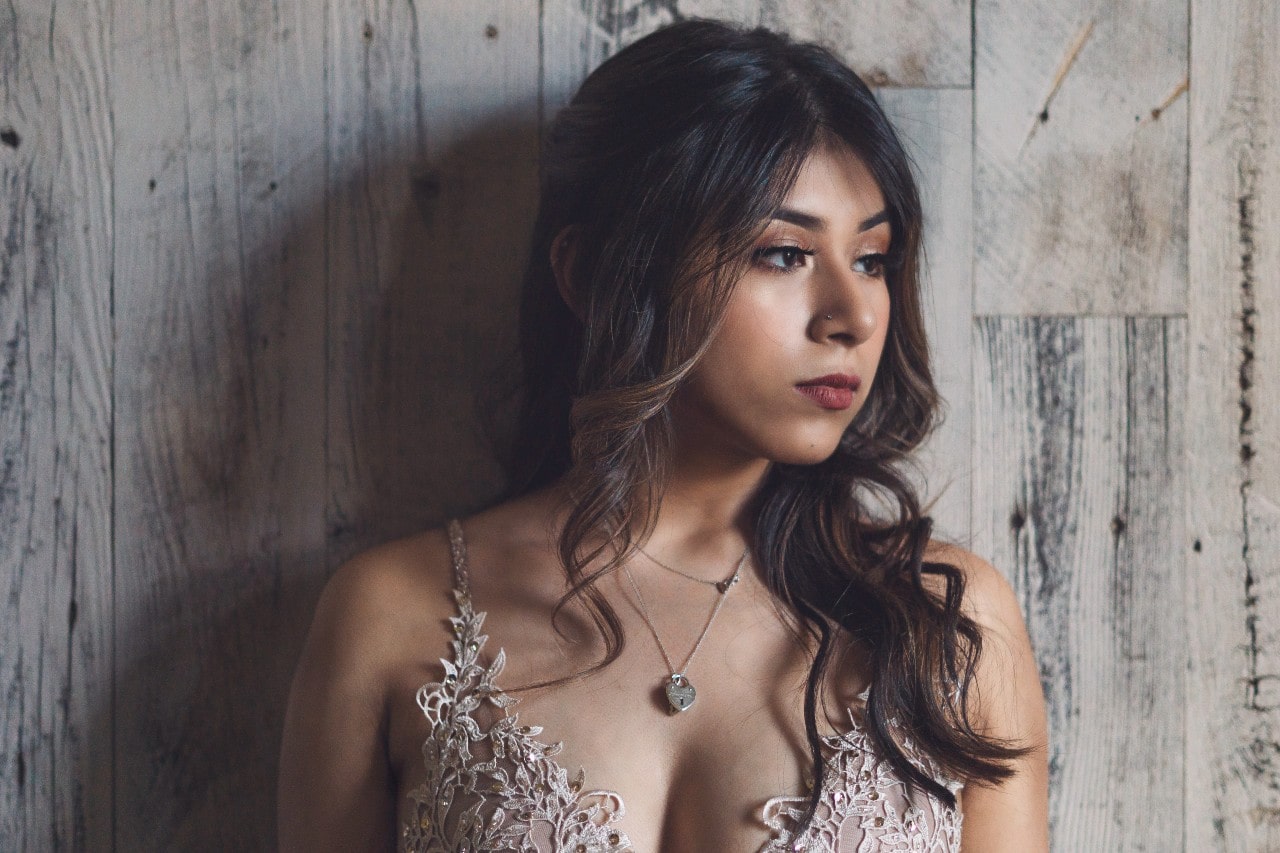 A close-up of a woman wearing a delicate diamond heart-lock pendant paired with an intricate lace-detailed dress.