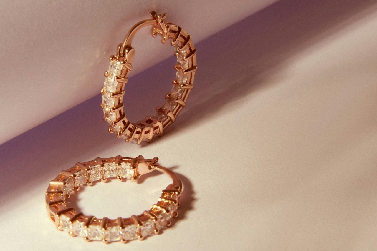 a pair of yellow gold hoop earrings with princess cut diamonds on a beige surface a pair of yellow gold hoop earrings with princess cut diamonds on a beige surface