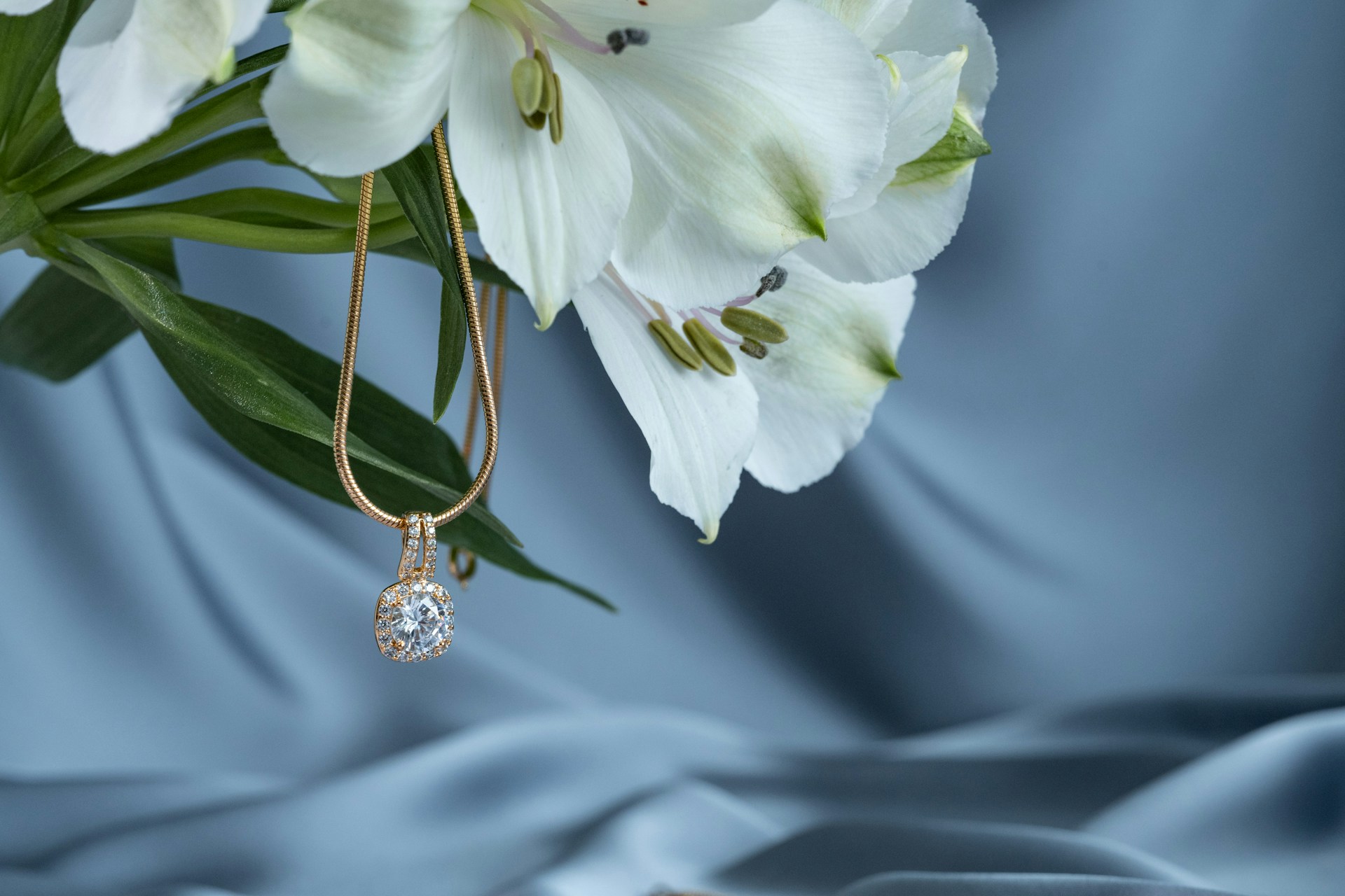 a yellow gold diamond pendant necklace hanging from a bouquet of white flowers a yellow gold diamond pendant necklace hanging from a bouquet of white flowers