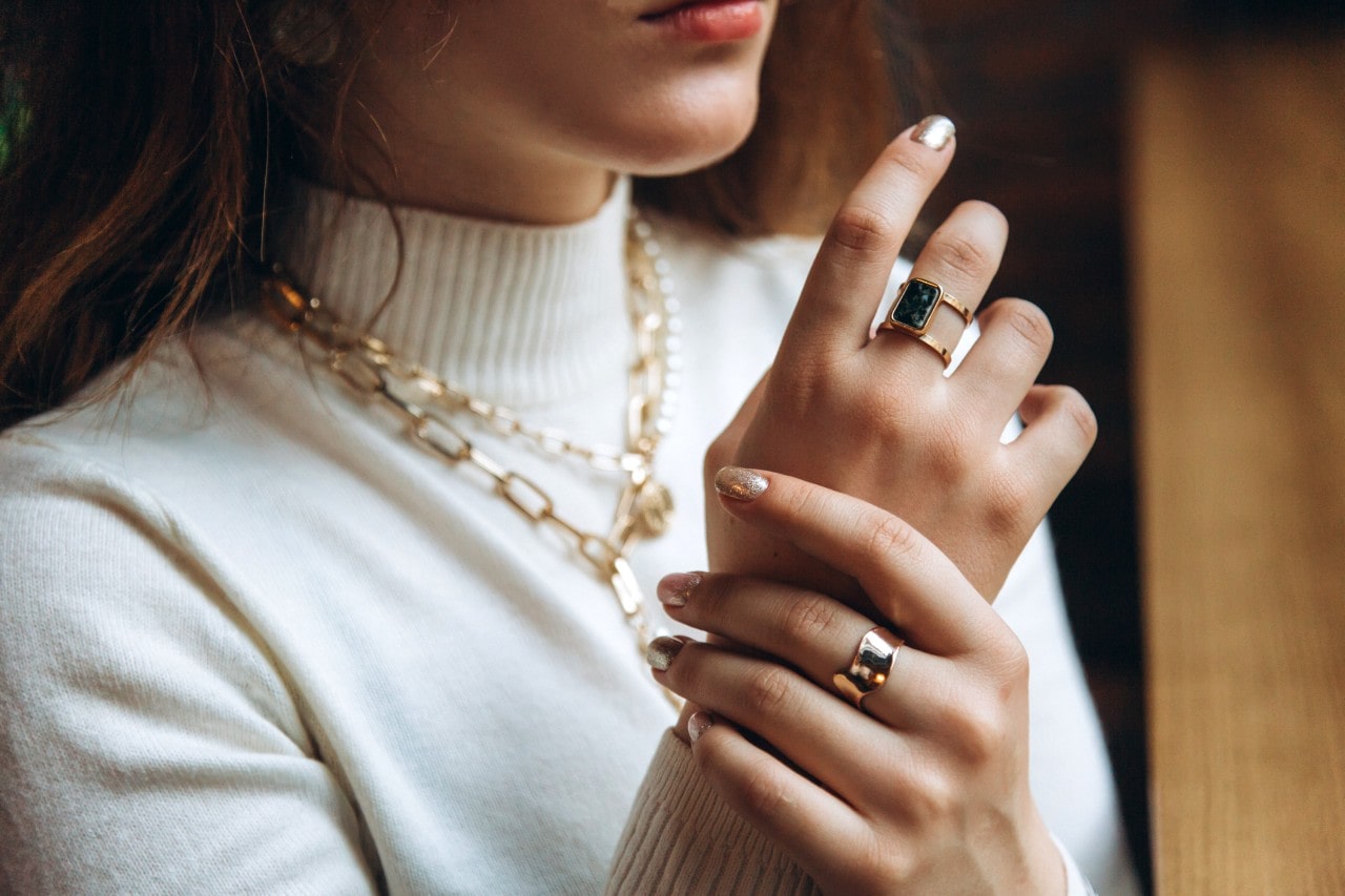 A woman in white turtleneck showcasing yellow gold chunky link necklace and statement rings