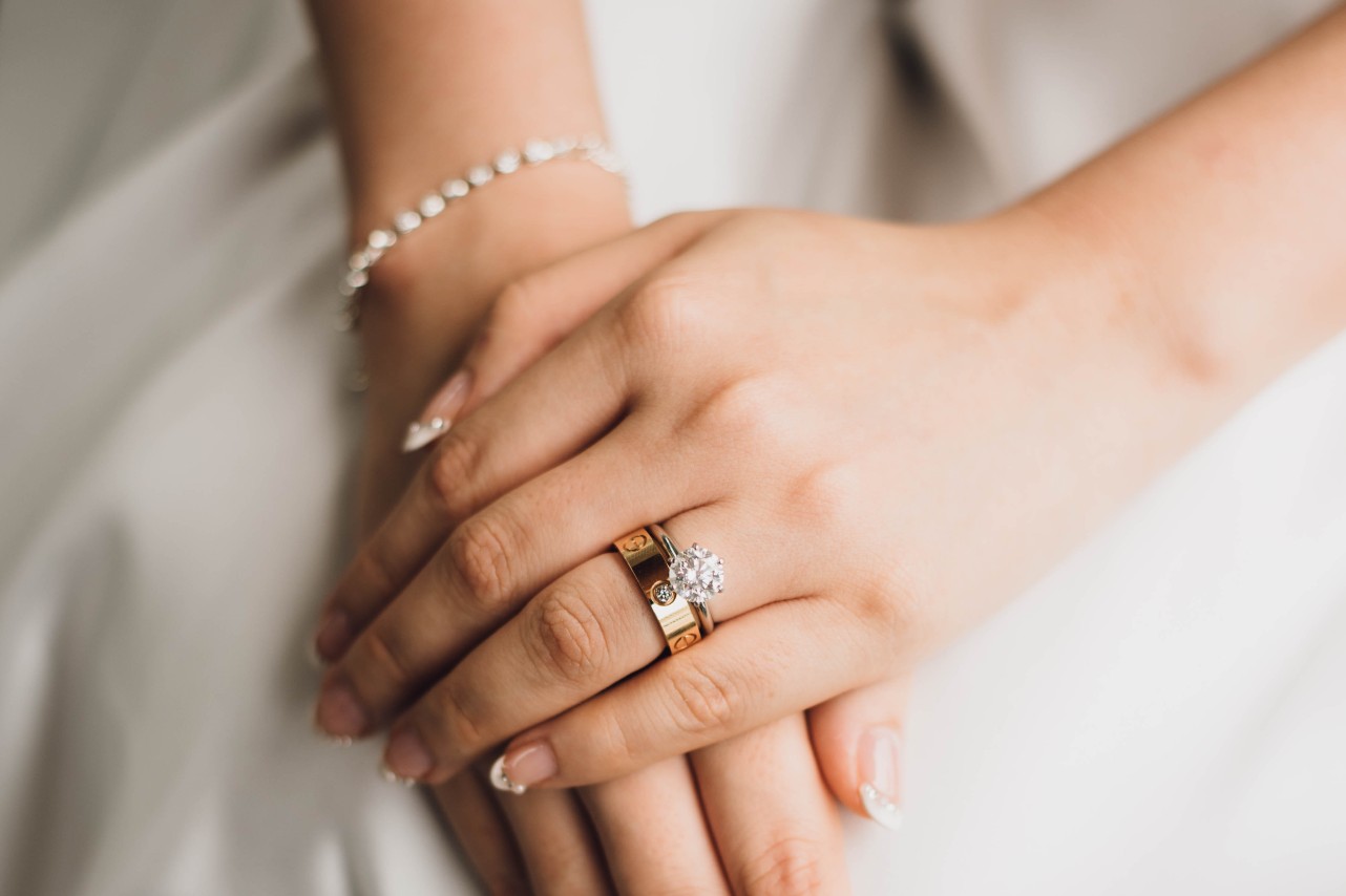 A close-up of a bride’s hands rested atop her lap, with emphasis on her engagement ring and wedding band stacked on her ring finger. A close-up of a bride’s hands rested atop her lap, with emphasis on her engagement ring and wedding band stacked on her ring finger.