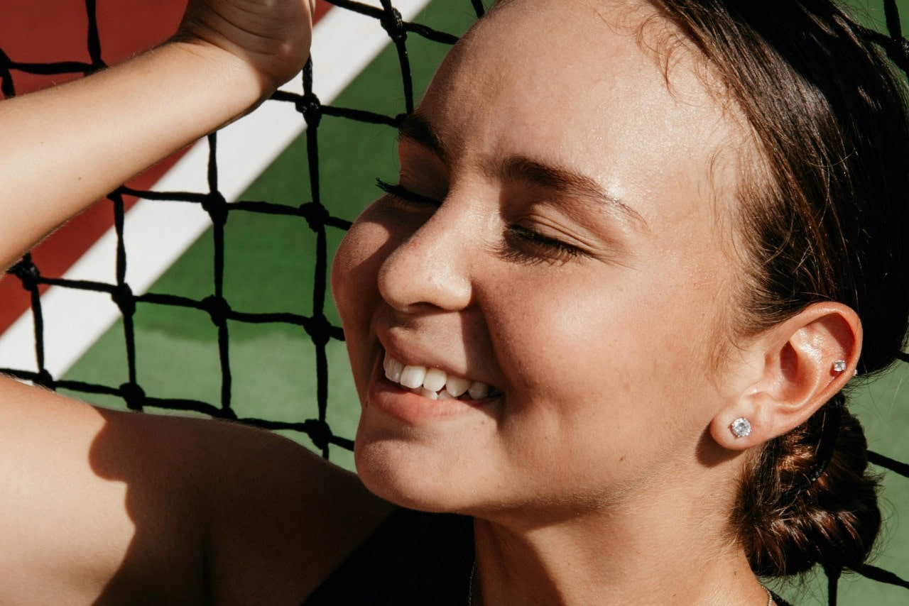 A smiling woman against a volleyball barrier net with a stud diamond earrings