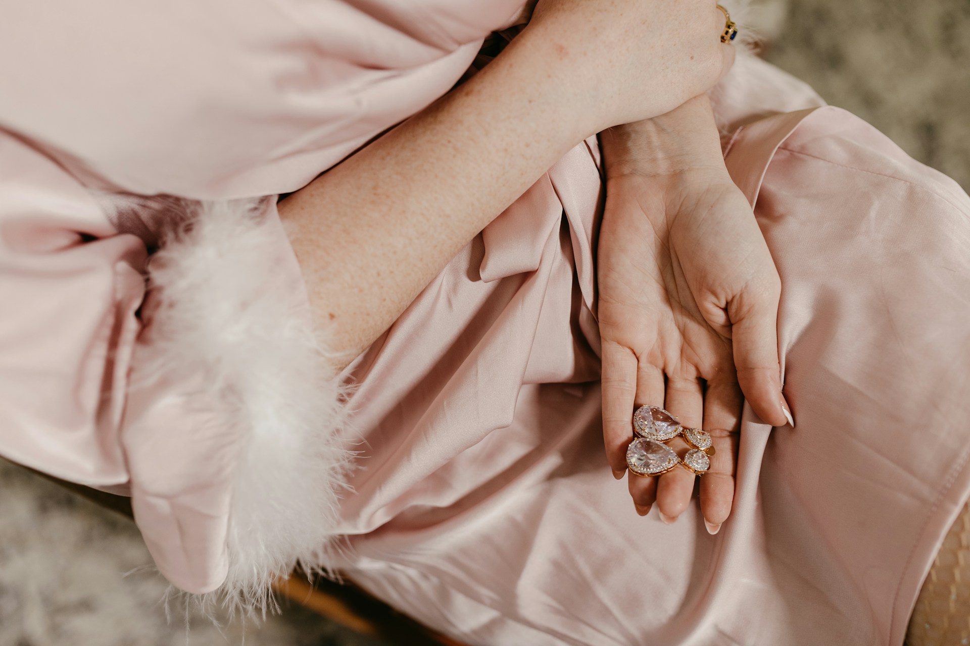 Women in a pink robe holding a drop diamond earrings on her palm