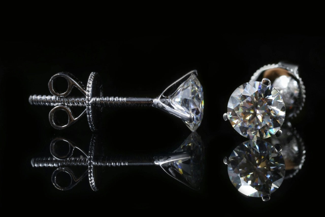 A close up of a white diamond stud earrings on a black reflective surface