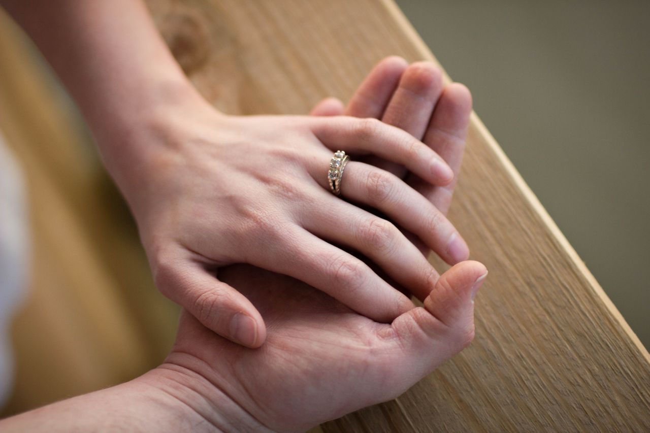 Close-up of two hands gently holding, with a woman’s hand on top, adorned with a diamond ring.