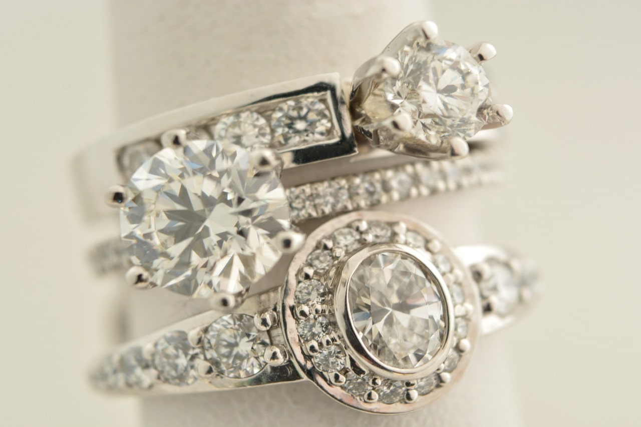 Close-up of three stacked diamond rings on a light background, showcasing various settings and sizes.