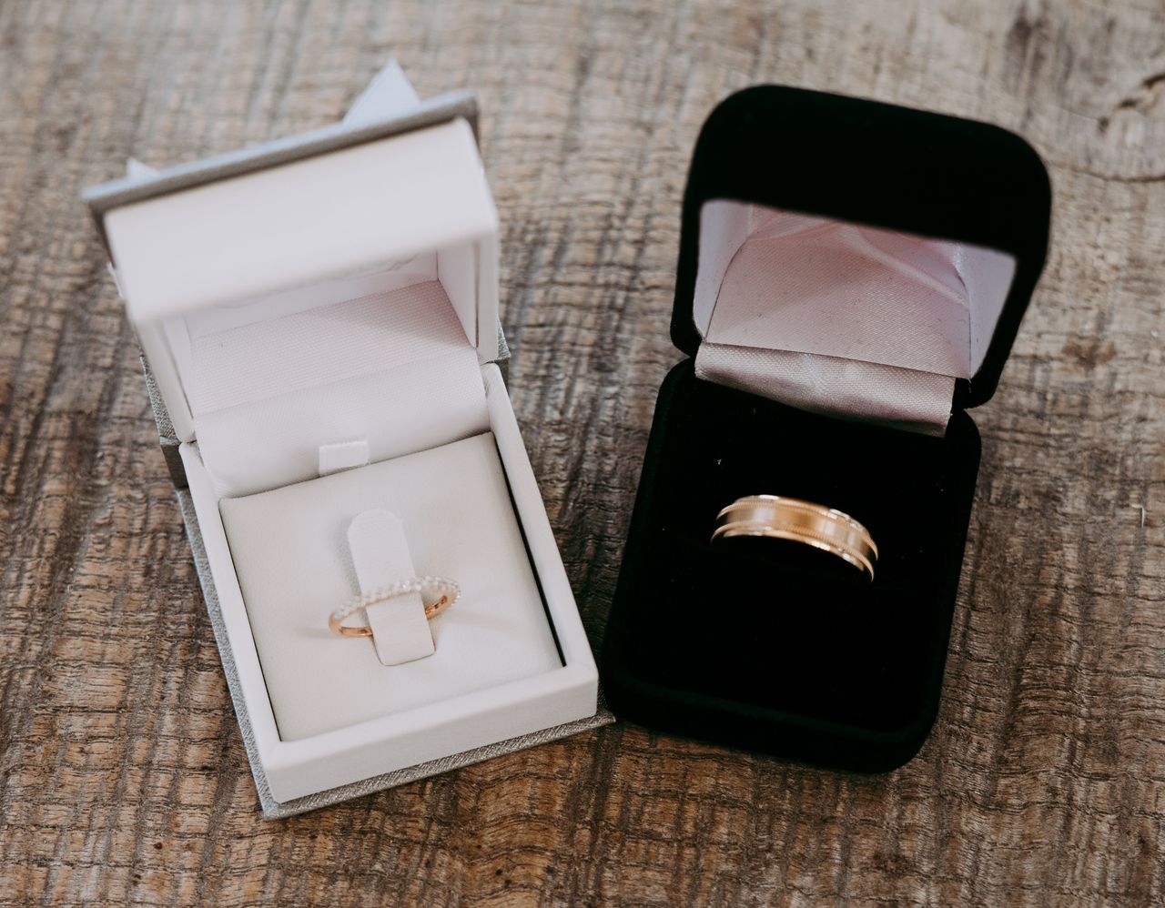 Two rings boxes, one black and one white, the black one holding a gold men’s wedding band and the white holding a thin gold and diamond women’s wedding band.