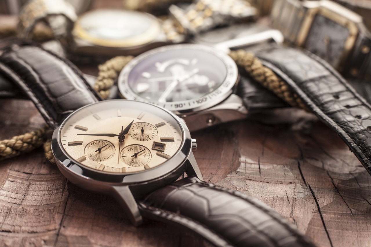 A close-up of wristwatches with brown leather straps resting on a rustic wooden surface. A close-up of wristwatches with brown leather straps resting on a rustic wooden surface.