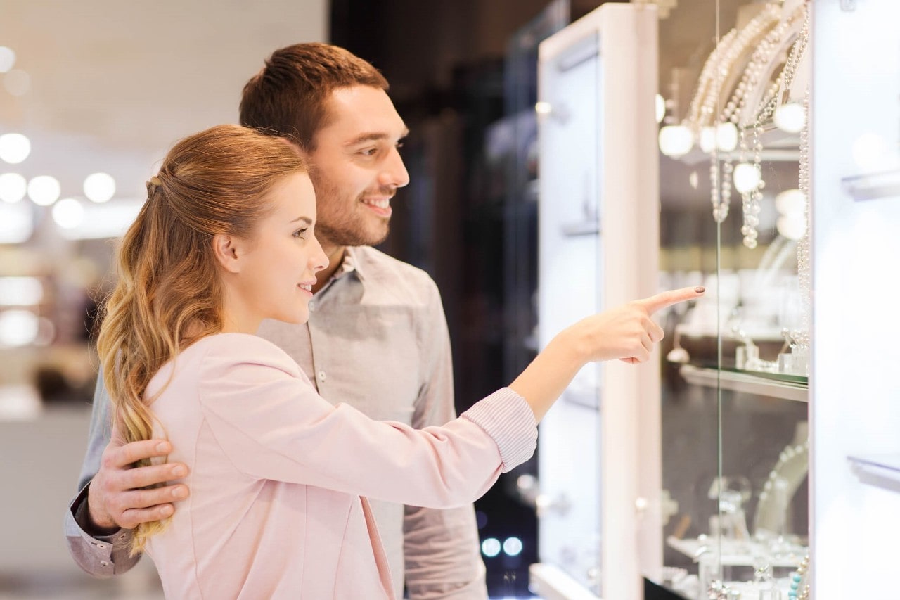 A smiling couple looking at a jewelry display in a luxurious boutique.
