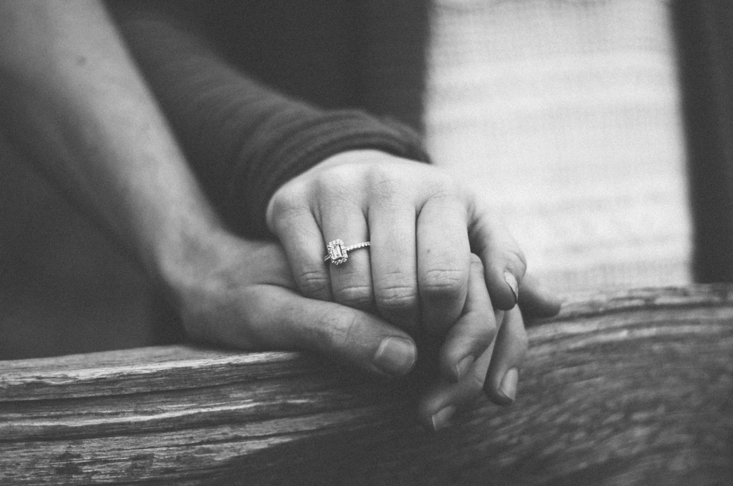 A black and white image of a couple holding hands, showcasing an emerald cut engagement ring.