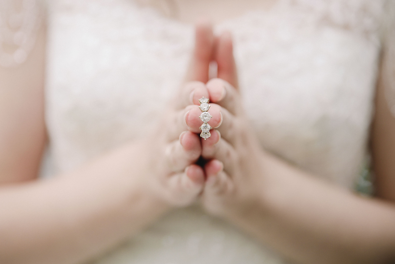 A bride holding a five stone engagement ring in between her two hands.