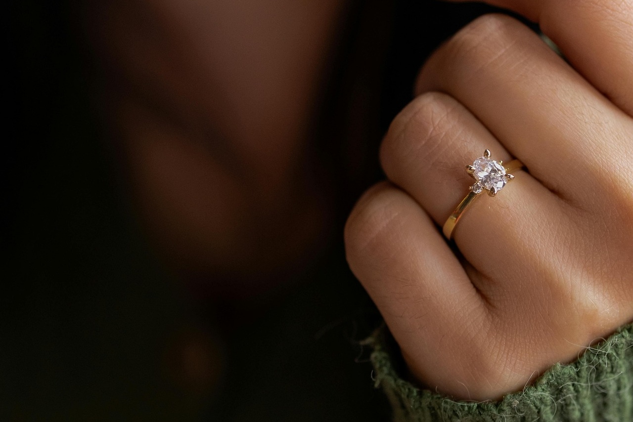 A close-up of a yellow gold solitaire engagement ring on a woman’s finger.