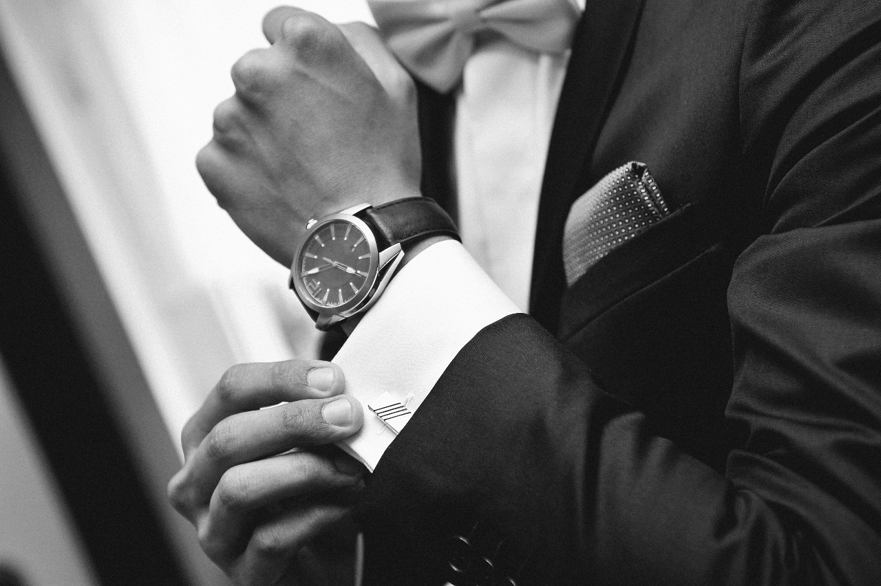 A black and white picture of a man fixing his cuffs and showcasing a massive leather wristwatch.