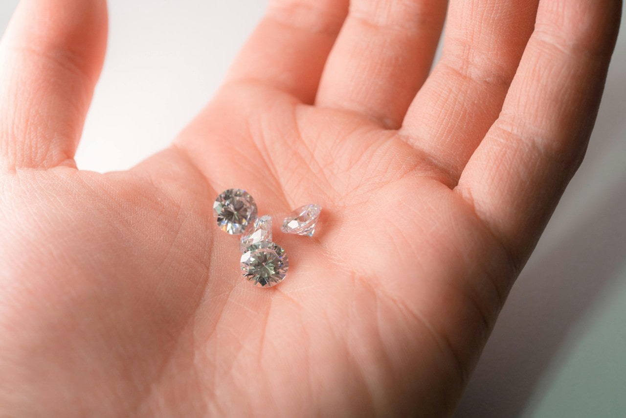 A close-up of a brilliant oval cut diamond shining while laying on a gray piece of fabric. A close-up of a brilliant oval cut diamond shining while laying on a gray piece of fabric.
