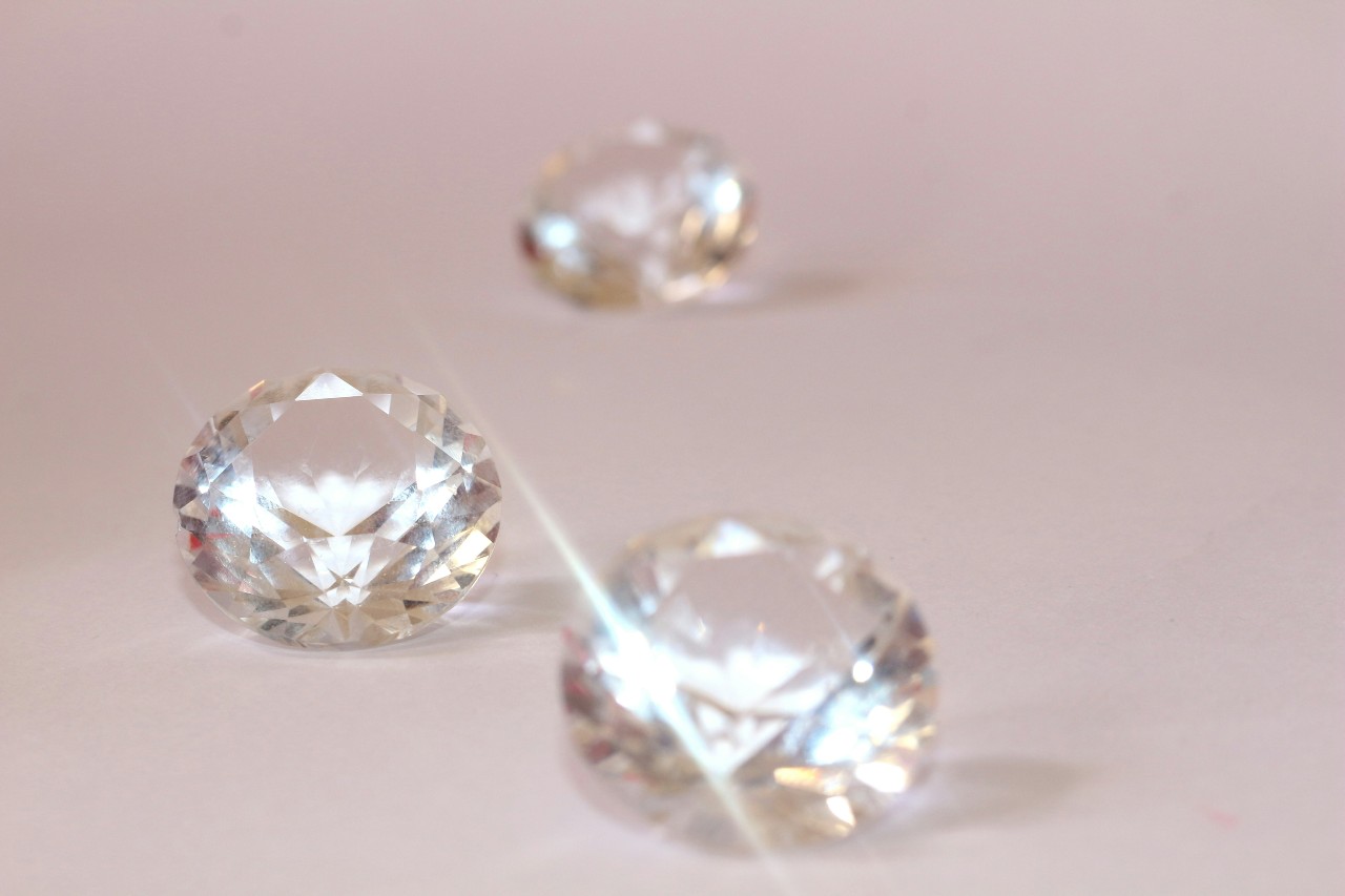 A close-up of three diamonds reflecting off each other, all sat on a baby pink surface. A close-up of three diamonds reflecting off each other, all sat on a baby pink surface.
