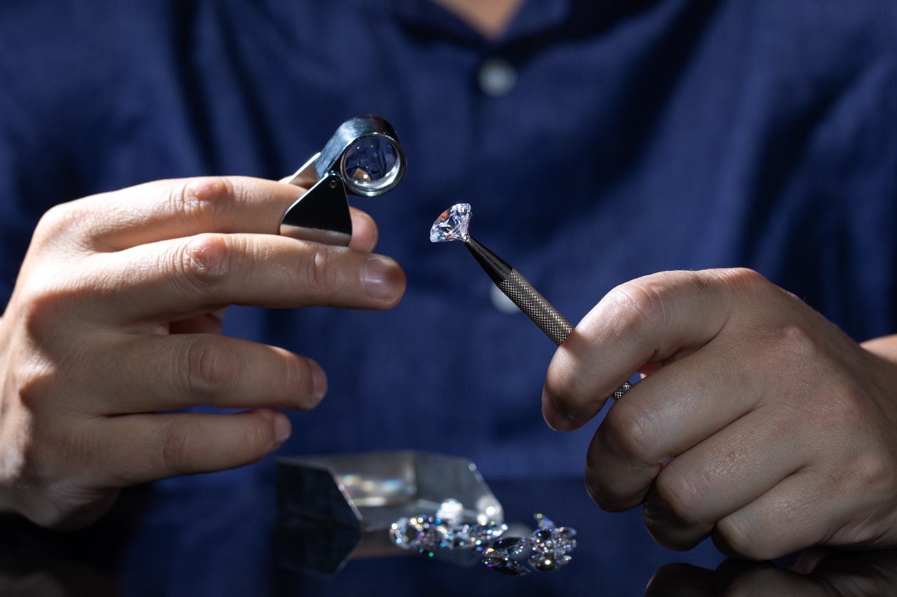 A close-up of a brilliant oval cut diamond shining while laying on a gray piece of fabric. A close-up of a brilliant oval cut diamond shining while laying on a gray piece of fabric.